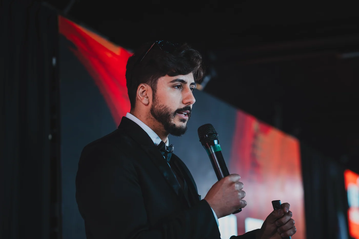 Gregori Oliveira de traje formal, falando ao microfone em um evento